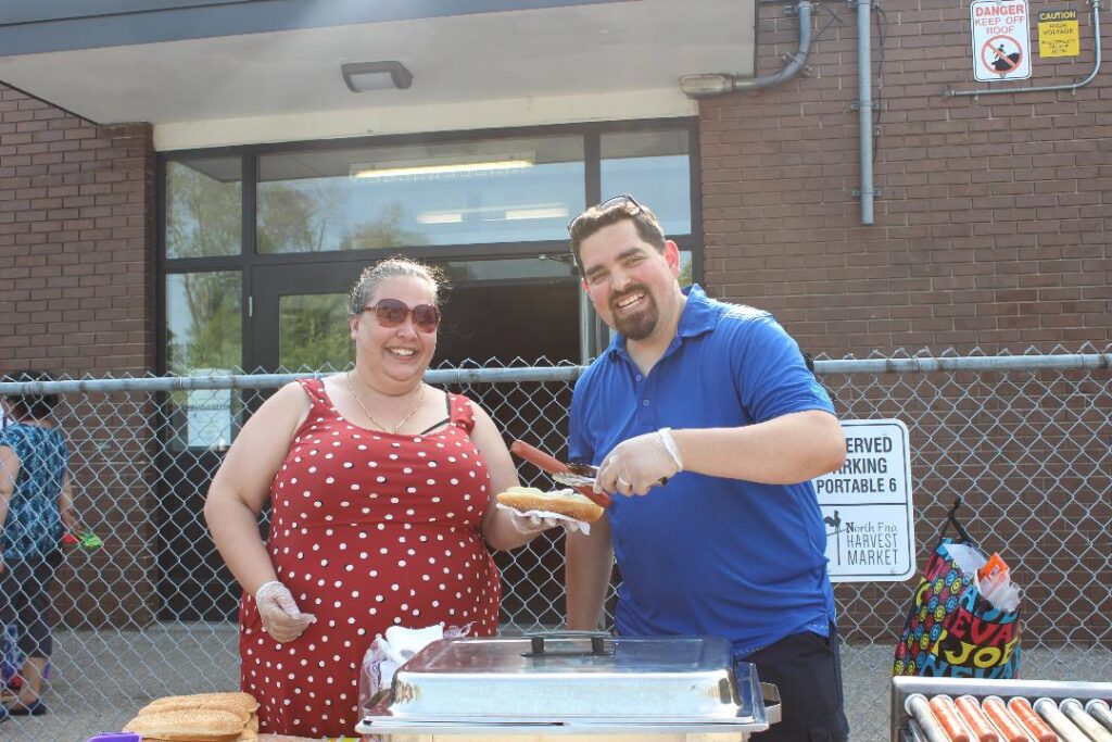 Rodrigo and Farrah at a community BBQ at the Waverley School parking lot. Rodrigo is helping Farrah assemble hotdogs.